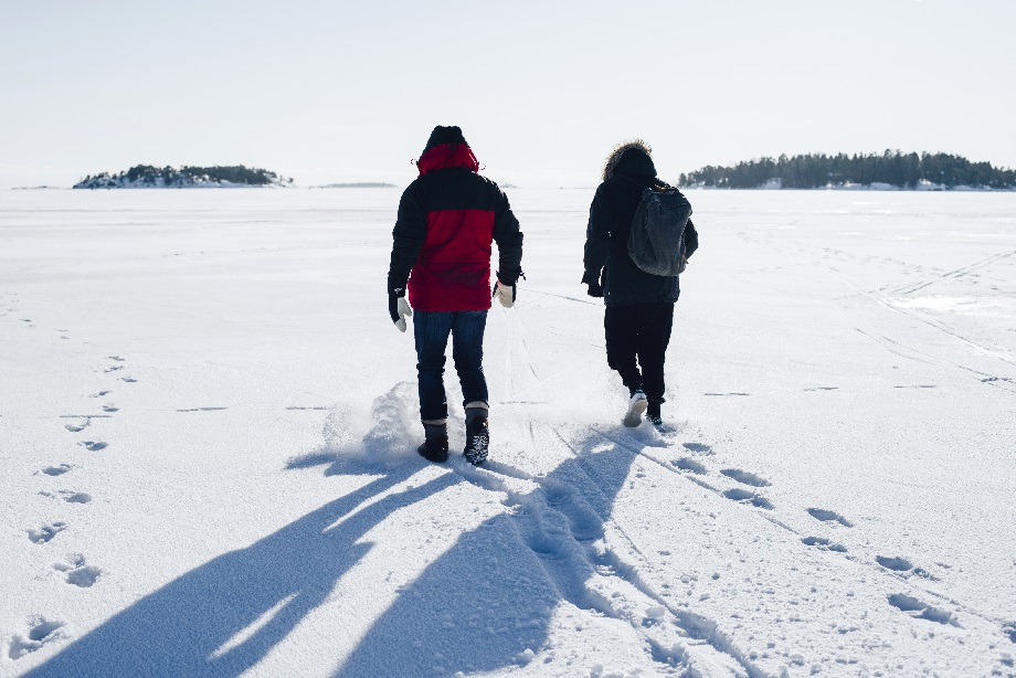 Kaksi henkilöä kävelee jäällä auringonpaisteessa selkä kameraan päin.