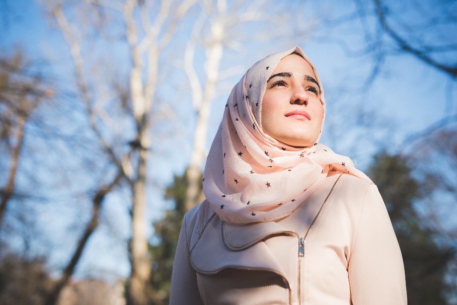 Valoisassa kuvassa nuori naisoletettu vaalenapunaisessa hijabissa katsoo levollisena eteenpäin, yläviistoon.