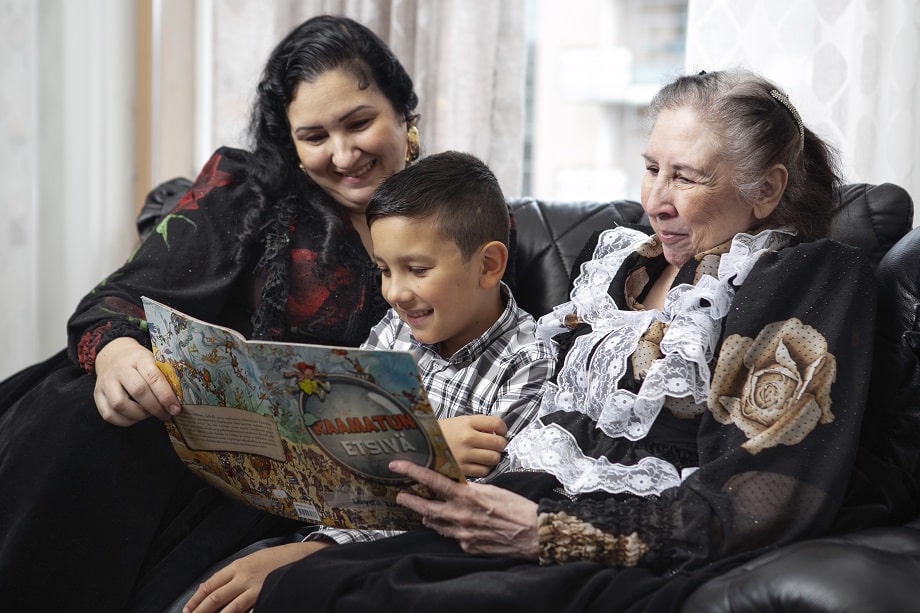 Romani lapset lukemassa kirjaa isoäidin kanssa.