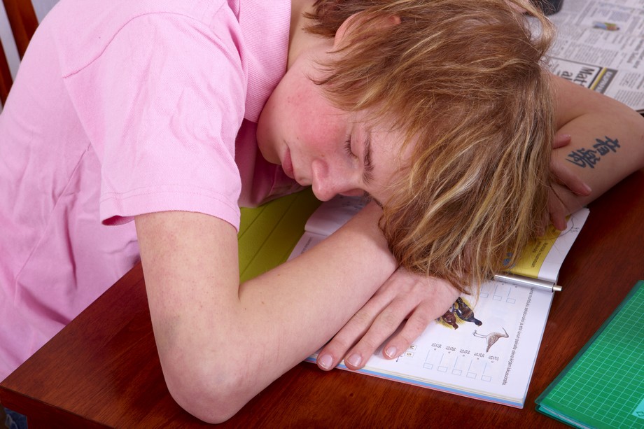 Nuori poika makaa silmät kiinni läksykirjan päällä.