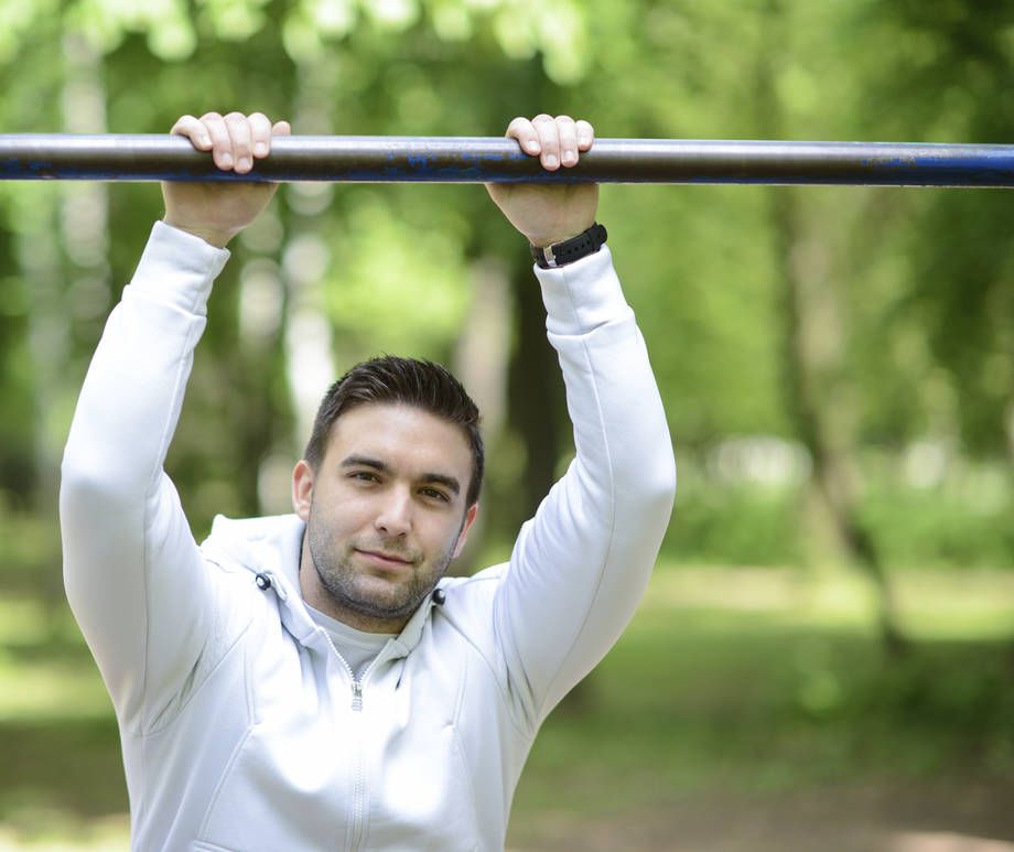 Mies pitää kiinni kaksin käsin yläpuolella olevasta tangosta ja katsoo kameraan.