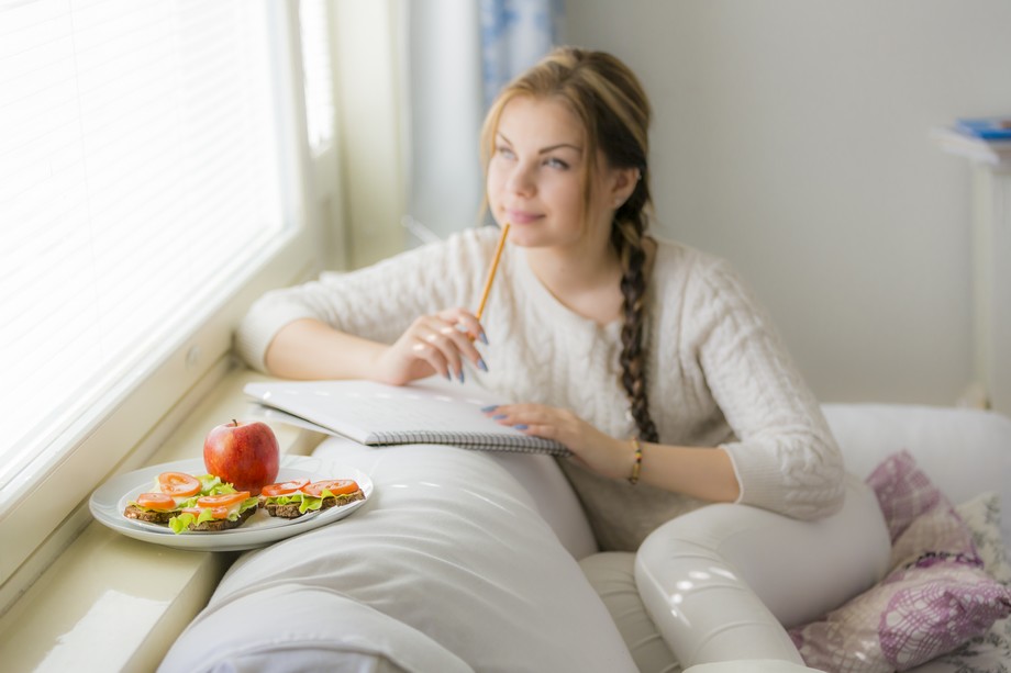 Nuori nainen istuu sohvalla miettien mitä kirjoittaisi, välipalalautanen vierellään.