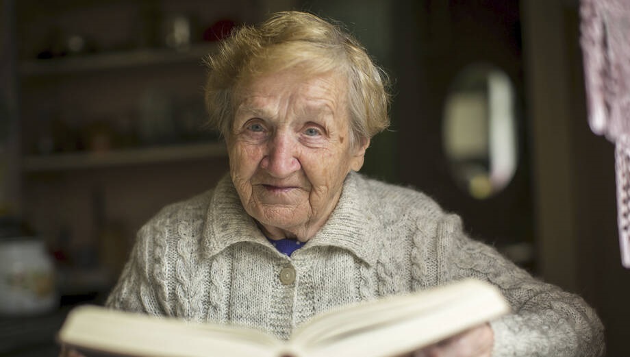Iäkäs nainen lukemassa kirjaa.