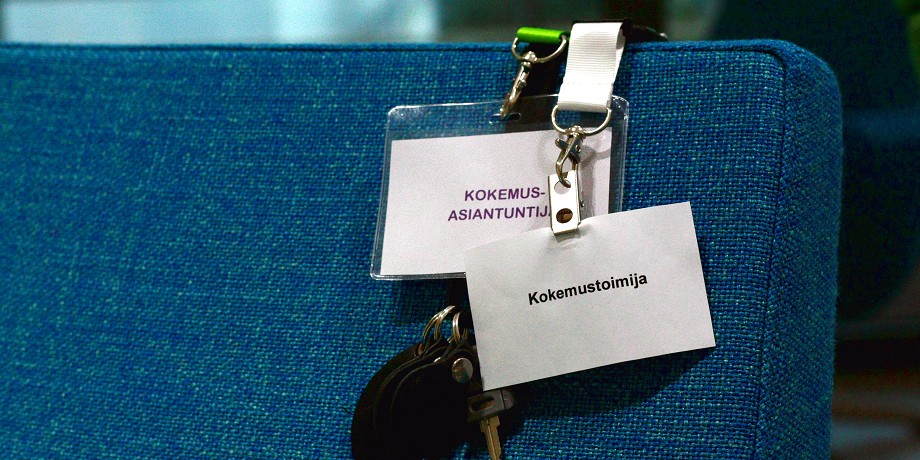 Kokemusasiantuntija- ja kokemustoimija-nimikyltit sohvan selkänojalla.