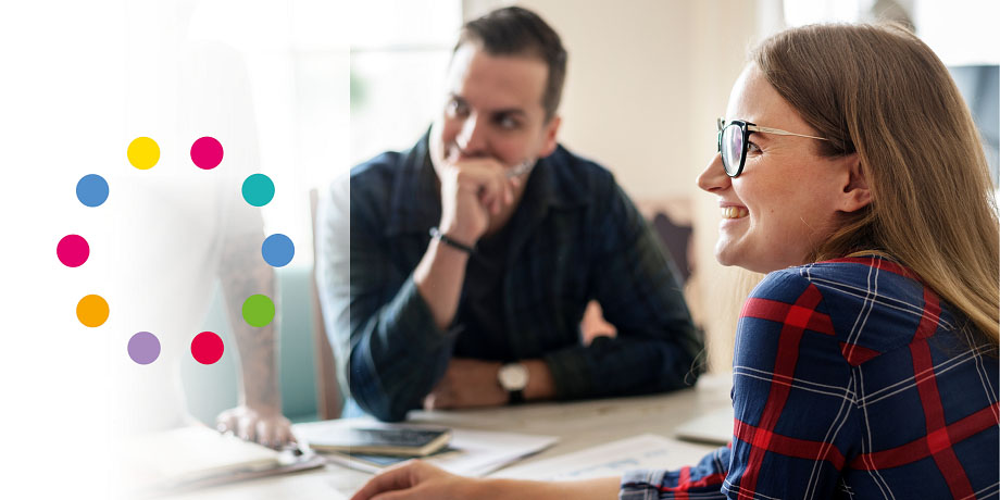 Nainen ja mies istuvat pöydän ääressä ja katsovat hymyillen kolmatta henkilöä.