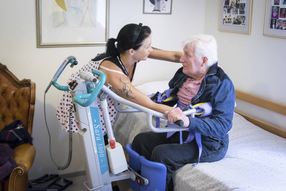 Tummatukkainen nainen auttaa vanhusta 