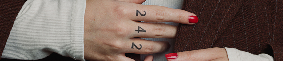 Naisen kädet, joissa sormiin tatuoitu numerot 2, 4 ja 2.