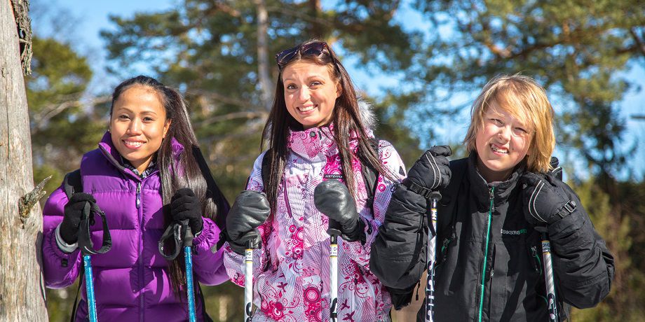 Kolme ihmistä hymyilee ulkona sauvakävelysauvat käsissään.