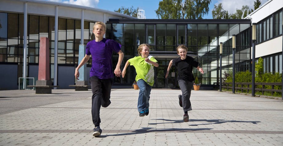 Kolme poikaa juoksee koulun pihalla