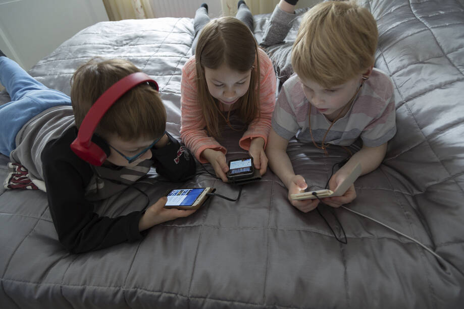 Kolme lasta sängyllä kännykät käsissä. 