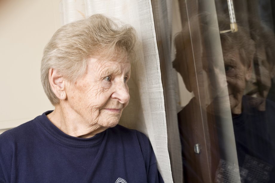 Iäkäs nainen katsoo ulos ikkunasta.