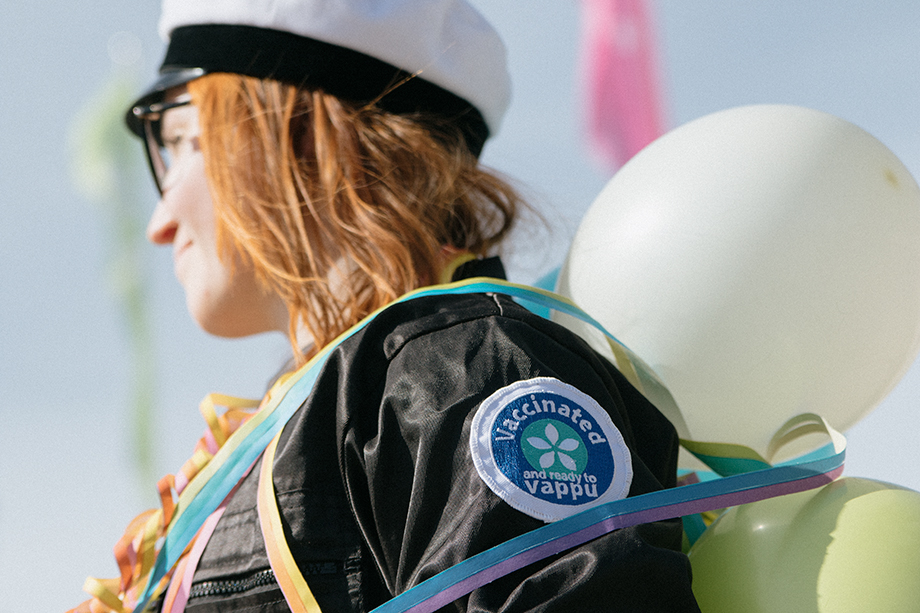 Nainen juhlimassa vappua ylioppilaslakki päässä ja haalareissa haalarimerkki "Vaccinated and ready to vappu".