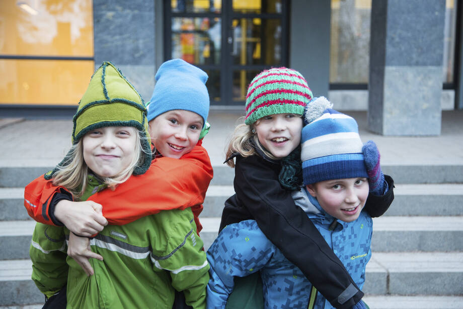 Neljä lasta hymyilee ja halailee koulun pihalla.