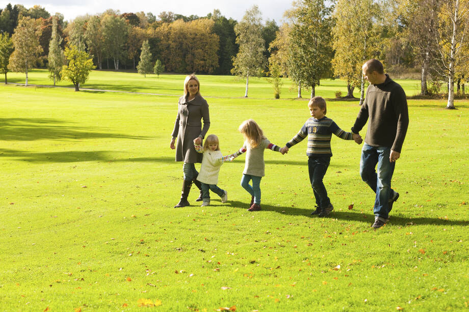 Perhe kävelee puiston nurmikolla käsi kädessä. 
