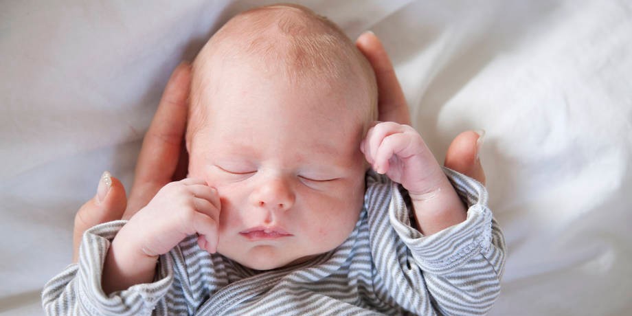 Vauva nukkuu vanhemman käsien varassa.