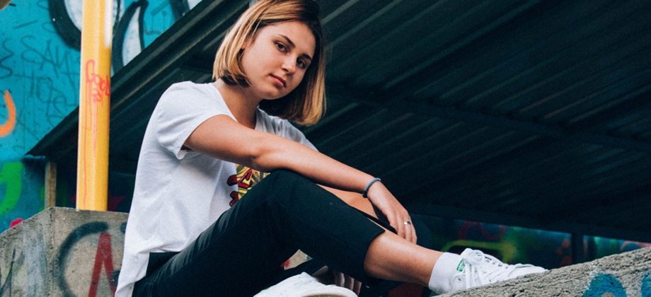 Tyttö istuu aidalla, taustalla graffiteja.