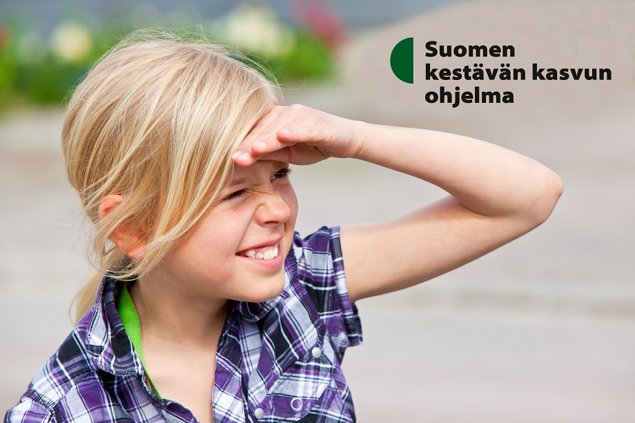 Hymyilevä lapsi suojaa katsettaan auringolta. Suomen kestävän kasvun ohjelma.