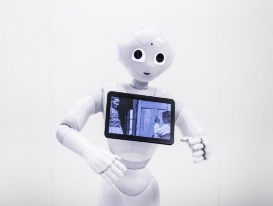 Ystävällisen näköinen robotti katsoo suoraan, rintakehässä on tabletti, jossa kuva kahdesta ihmisestä.