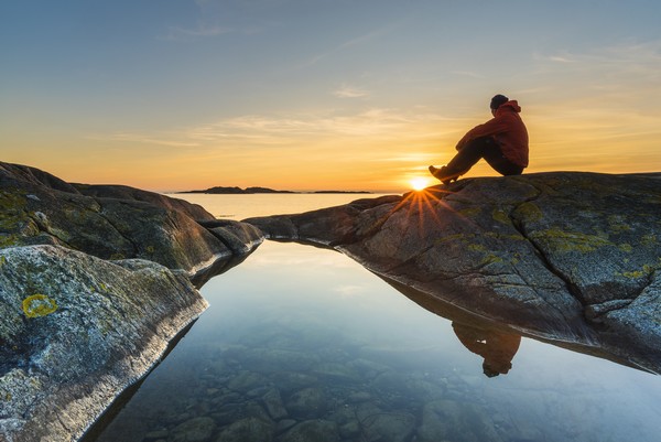 Aikuinen katsoo auringonlaskua rannalla.