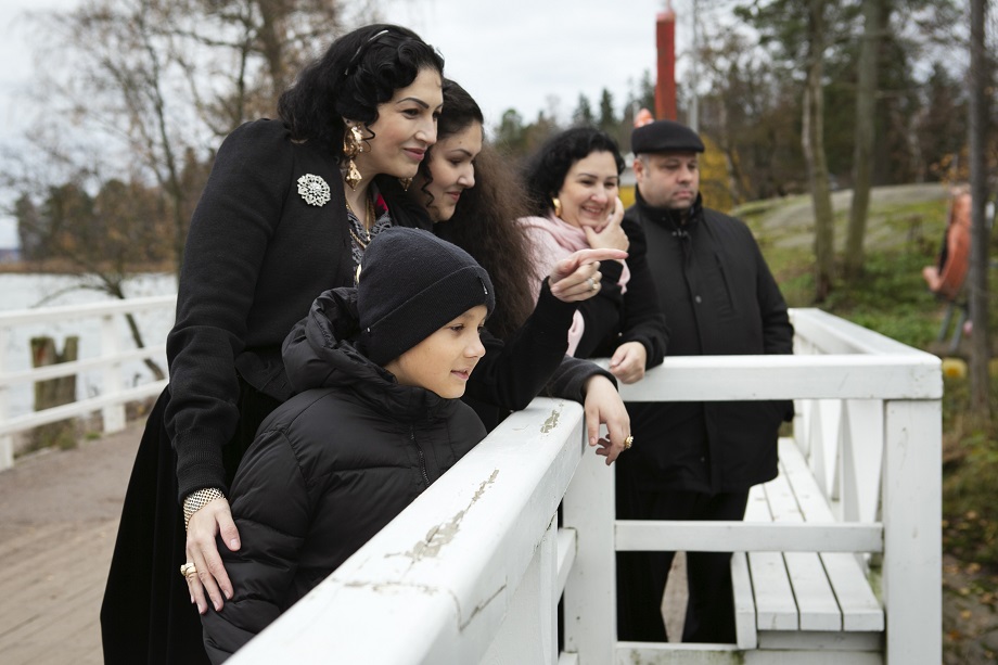 Eri-ikäisiä romaniperheen jäseniä katsoo hymyillen sillalta.