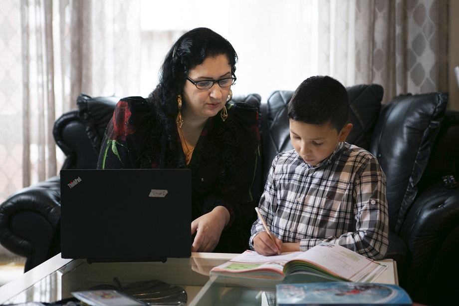 Romaninainen istuu tietokoneella ja auttaa poikaa läksyjen teossa.