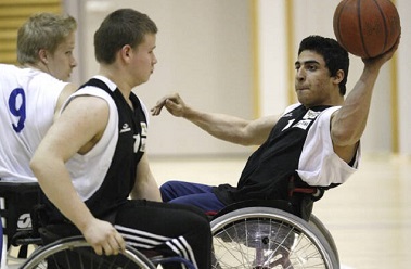Nuoret miehet pelaavat koripalloa pyörätuolissa.