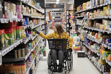 Nainen kaupan teehyllyn ääressä pyörätuolissa.