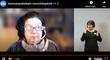 Nainen pitää puheenvuoroa etäyhteydellä. Vieressä viittomakielen tulkki.