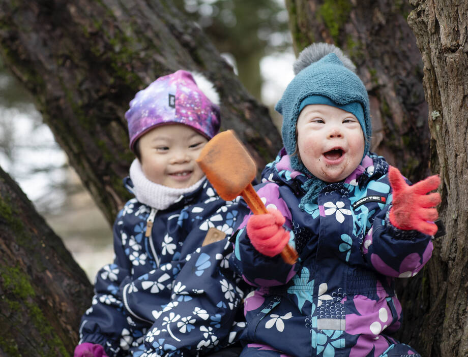 Kaksi lasta nauraa ja istuu puun juurella toppapuvuissa