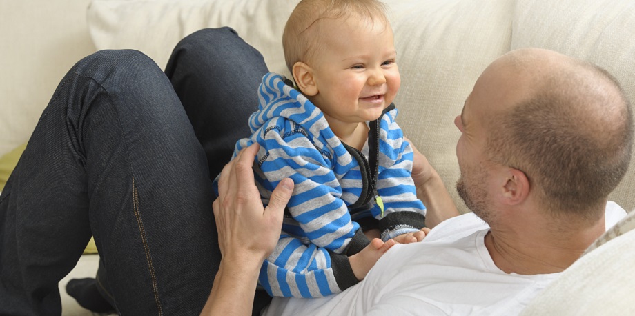 Vauva nauraa isän mahan päällä sohvalla.