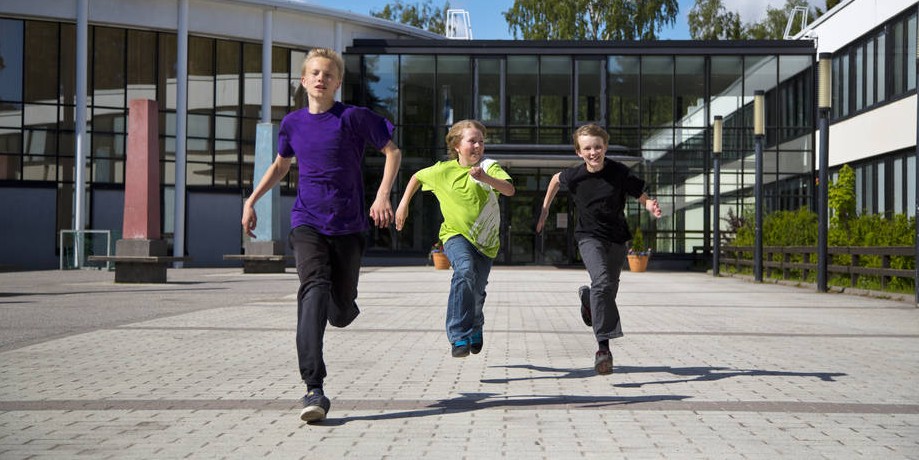Pojat juoksevat koulun pihalla.