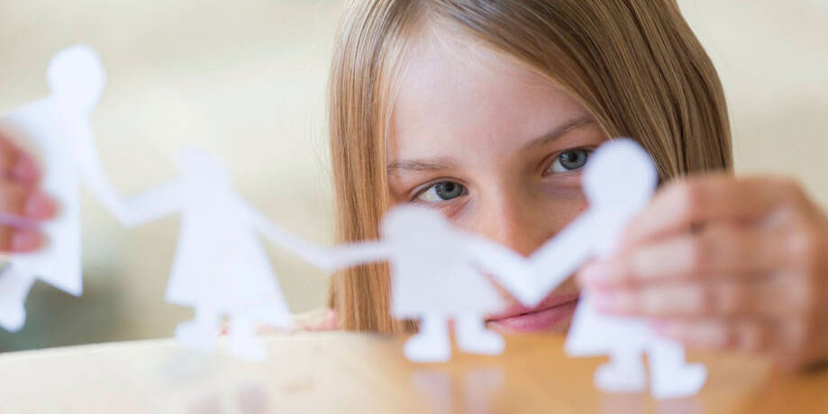 tyttö asettelee paperisia ihmishahmoja pöydälle.