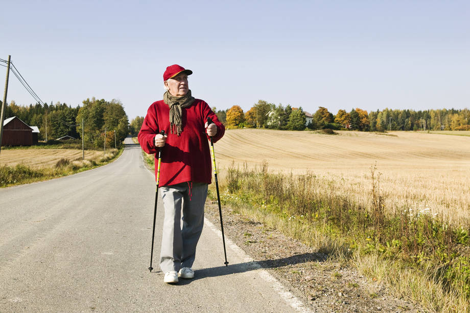 Vanha mies sauvakävelyllä syksyisessä peltomaisemassa.