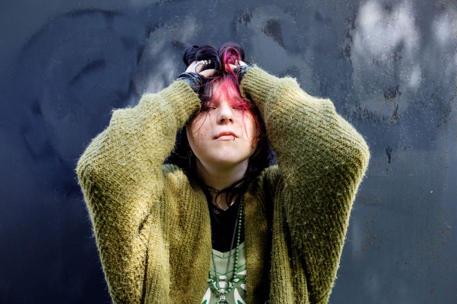 Nuori on laskenut kädet hiuksiinsa ja katsoo kameraan.