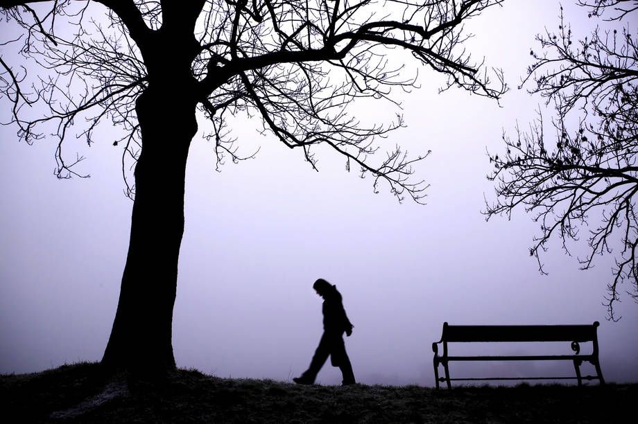En människa går eftertänksamt i en dimmig park.