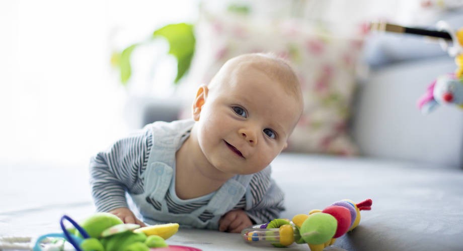 lapsi makaa vatsallaan lattialla ja hymyilee.