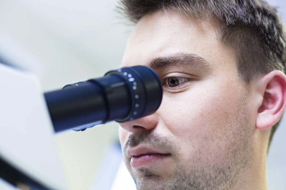 mies katsoo mikroskooppiin.