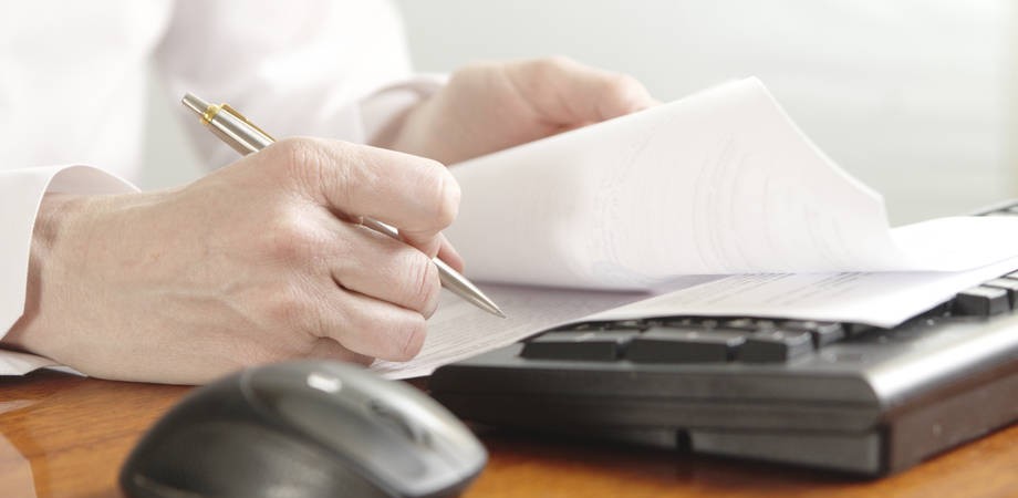 ihminen selaa papereita tietokoneen edessä.