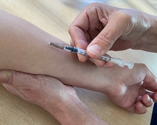 Rokotettavan ihoa kiristetään kyynärvarren alapuolelta ennen rokottamista.