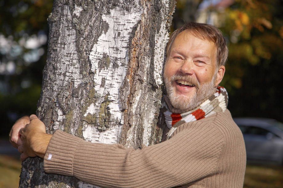 Smiling man hugs a birch tree.