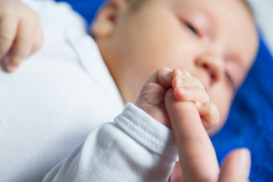 Bebisen håller i förälderns finger.