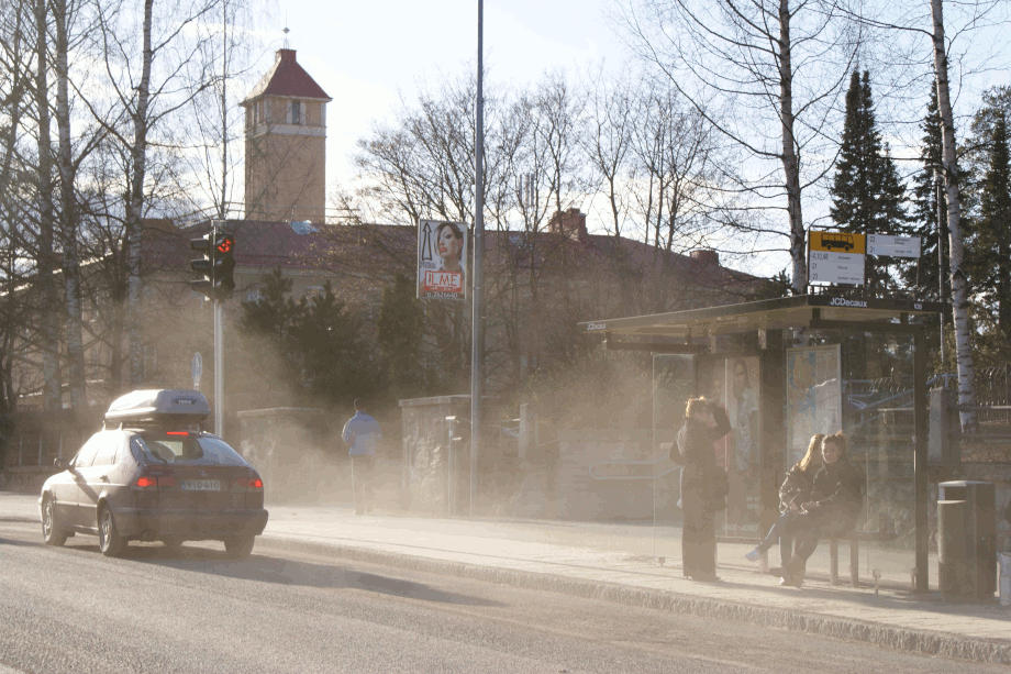 Auto nostaa ilmaan katupölyä bussipysäkillä.