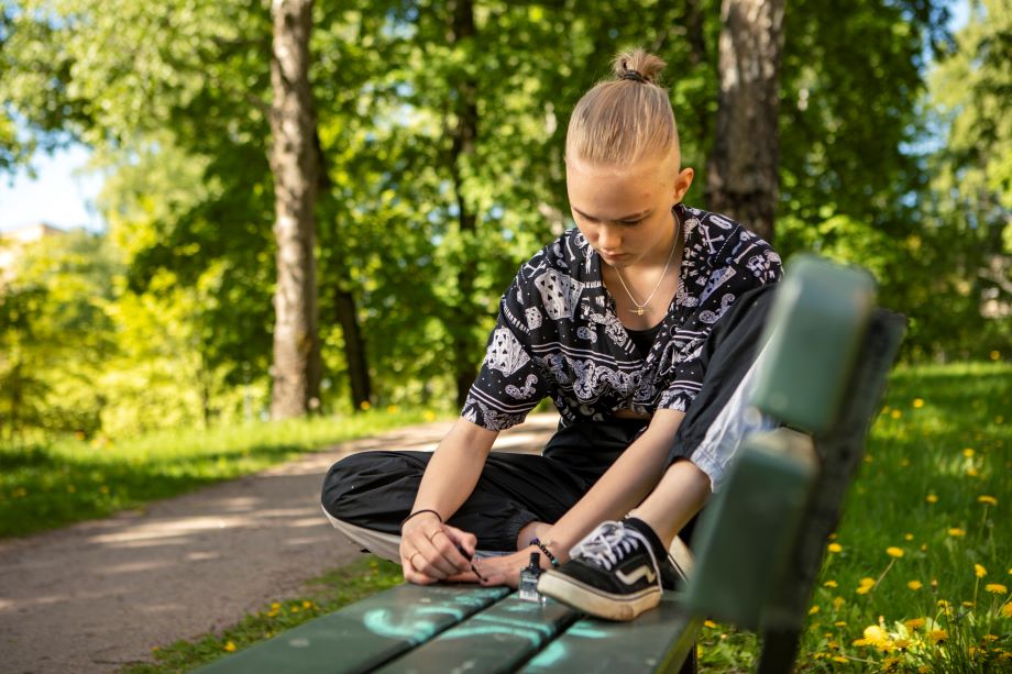 En ungdom lackar naglarna i parken.