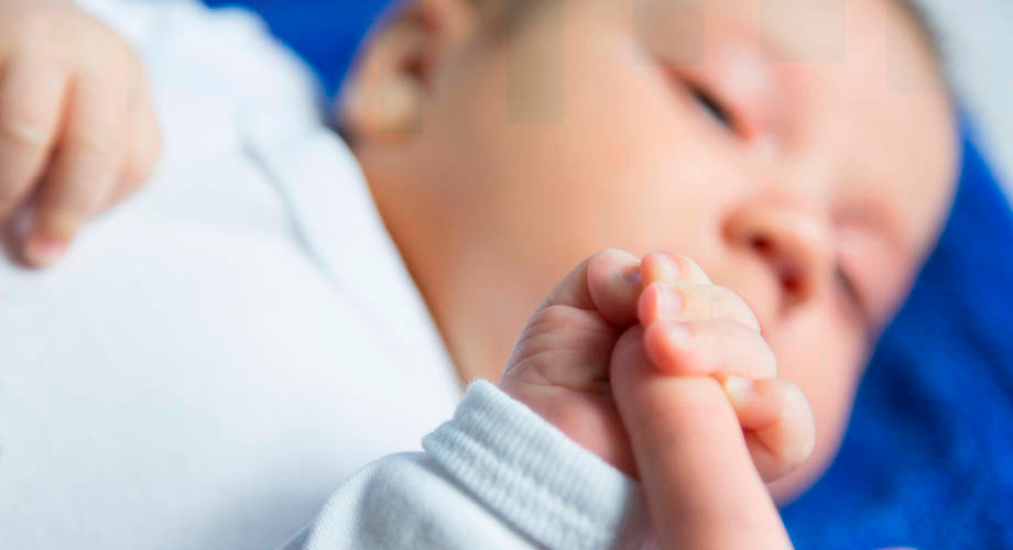 Baby holds adult finger.